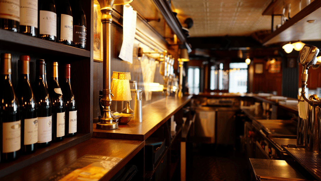 Cozy French bistro bar with bottles of wine, brass fixtures, and warm amber lighting against dark wood shelves