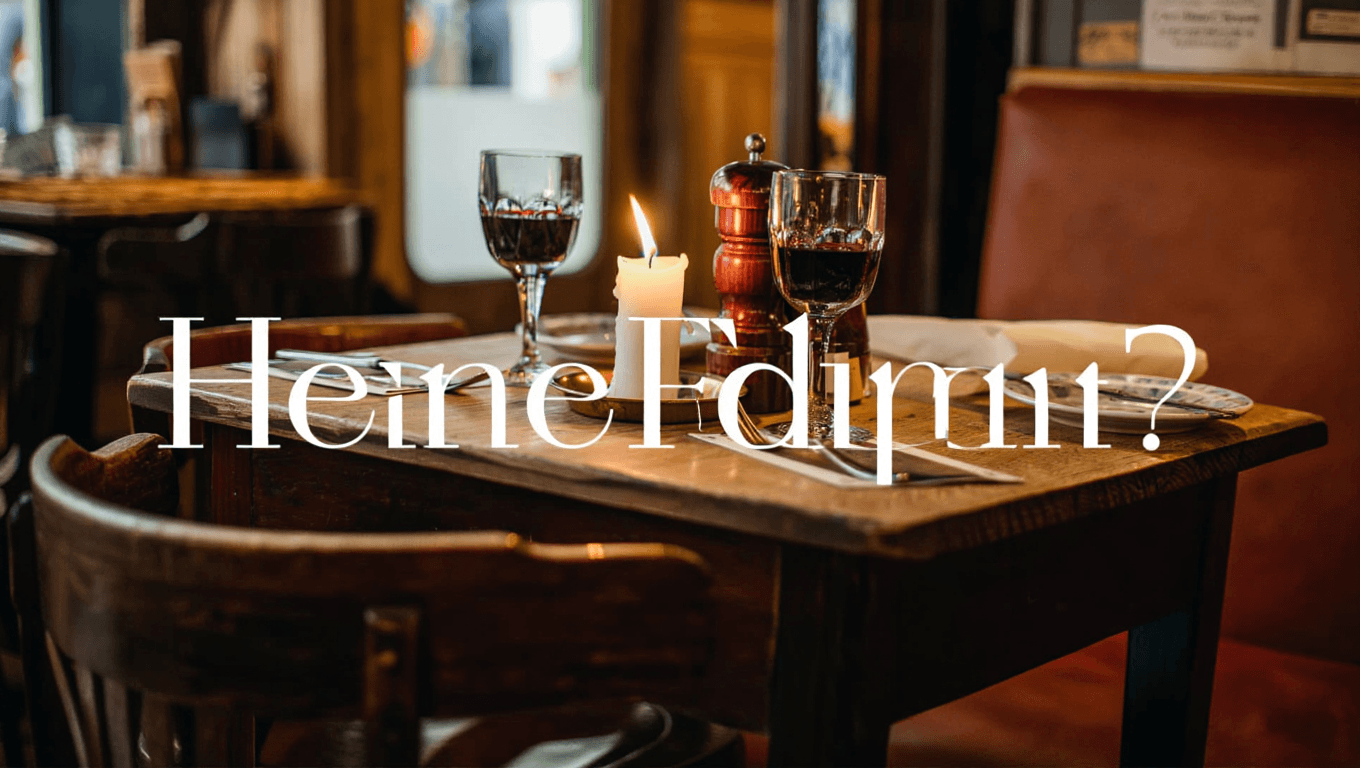 Intimate French bistro table setting with a lit candle, two glasses of red wine, and linen napkins on dark wood