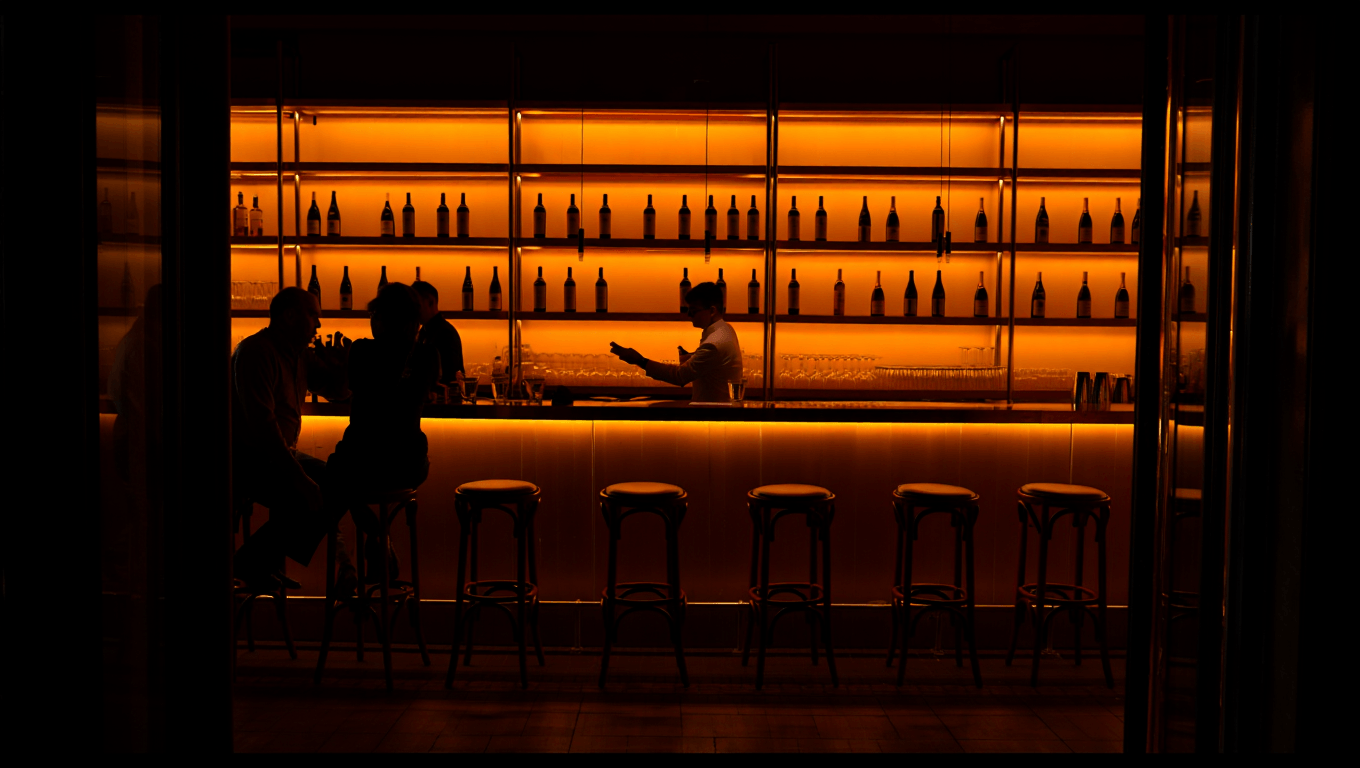 Cozy French bistro bar area with bottles of wine on wooden shelves and warm amber backlight