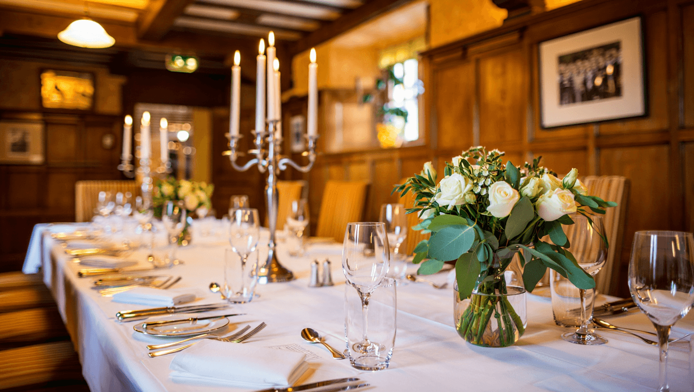 Elegant private dining table set for a celebration with candles, fine glassware, and floral accents in a warm wood-paneled room